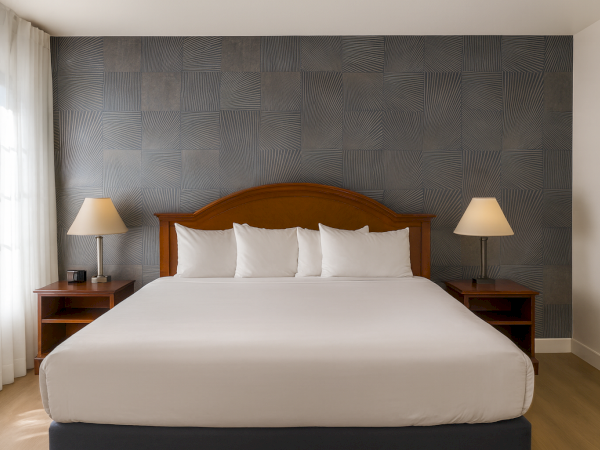 A modern hotel room with a large bed, wooden headboard, two nightstands, matching lamps, and a textured accent wall behind the bed, bright and airy.