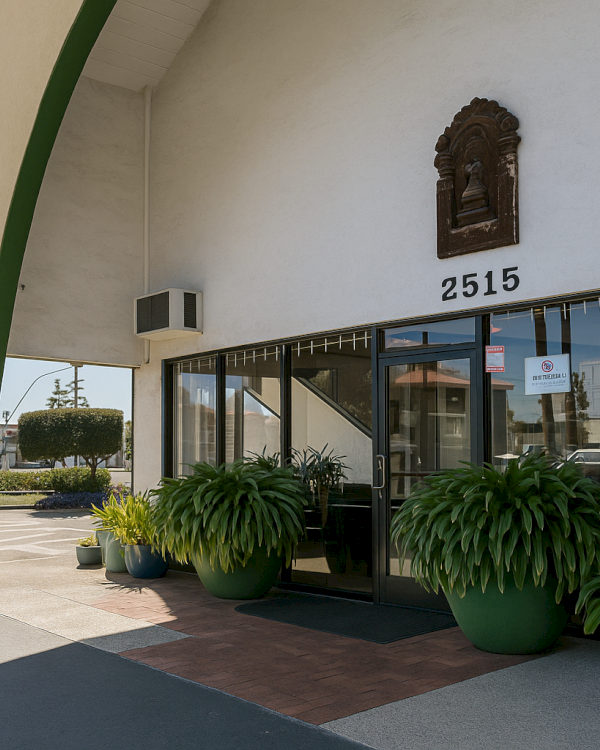 A storefront with large glass windows, arched green support, potted plants by the entrance, and the number 2515 above the door.