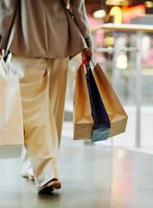 A person is shopping, carrying multiple shopping bags in both hands as they walk through a mall.