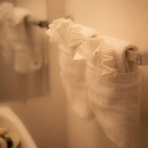 A close-up of a hand towel rack with white towels hanging on a towel bar in a bathroom, soft lighting, sink and toiletries in the blurred background.